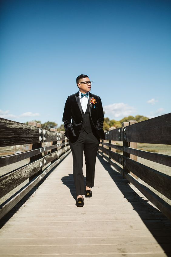 a velour jacket tux, a blue bow tie, a bold boutonniere and black embroidered velvet loafers for a dashign touch