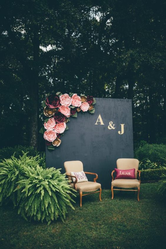 an elegant photo booth with a black and monogram backdrop decorated with paper flowers and refiend chairs