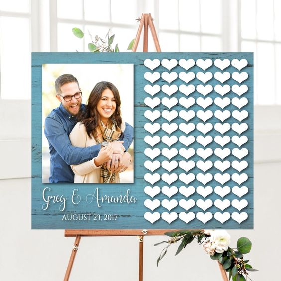 a stylish wedding guest book of a blue wooden sign, a large couple photo and lots of wooden hearts attached