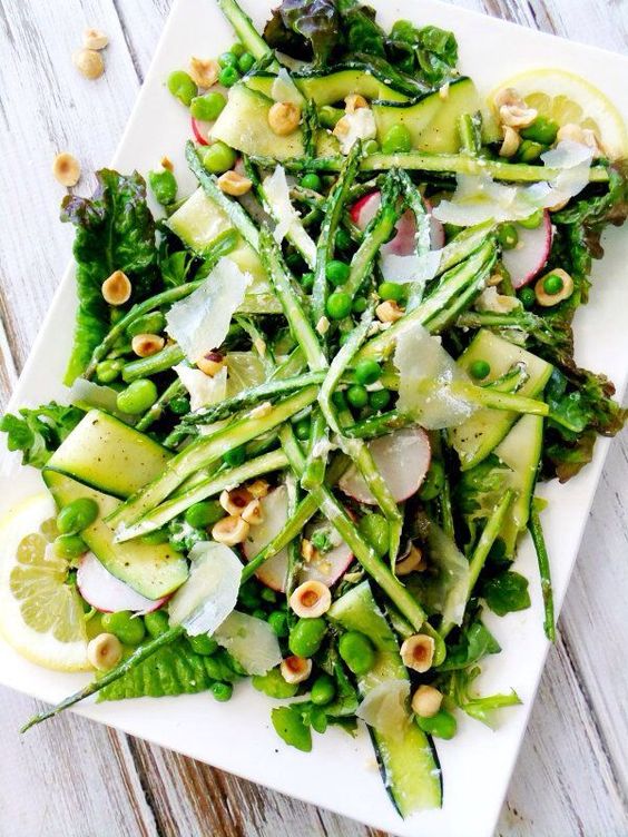 a spring salad of zucchini ribbons, red leaf lettuce, sliced radishes, shaved asparagus spears, peas, fava beans, hazelnuts, lemon wedges and Parmesan shavings