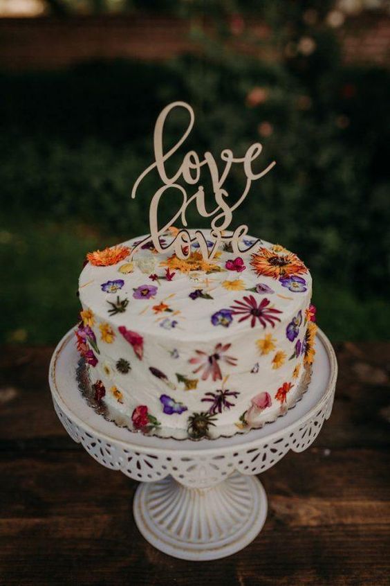 a beautiful wedding cake with edible fwildflowers in the icing and a calligraphy cake topper
