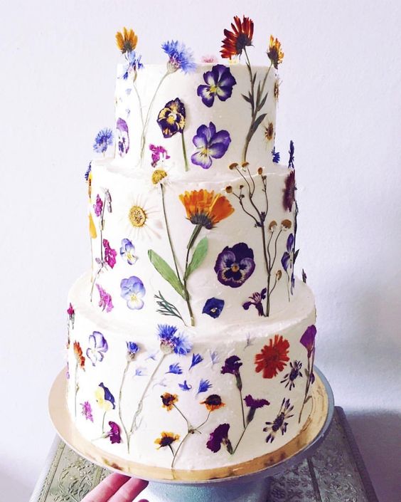 a pure white wedding cake all decorated with edible blooms looks wild and very chic