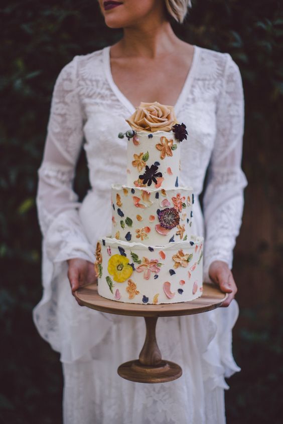 a boho chic wedding cake with painted and pressed blooms plus a single bloom on top