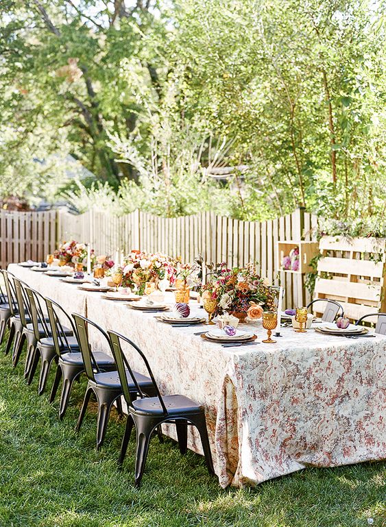 a cozy vintage rustic table setting with lush centerpieces and colored glasses plus vintage chairs