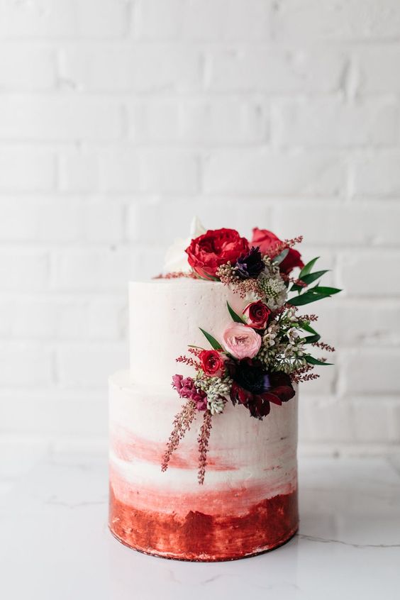 a bright ombre wedding cake in white to pink plus red, pink ad burgundy blooms and greenery