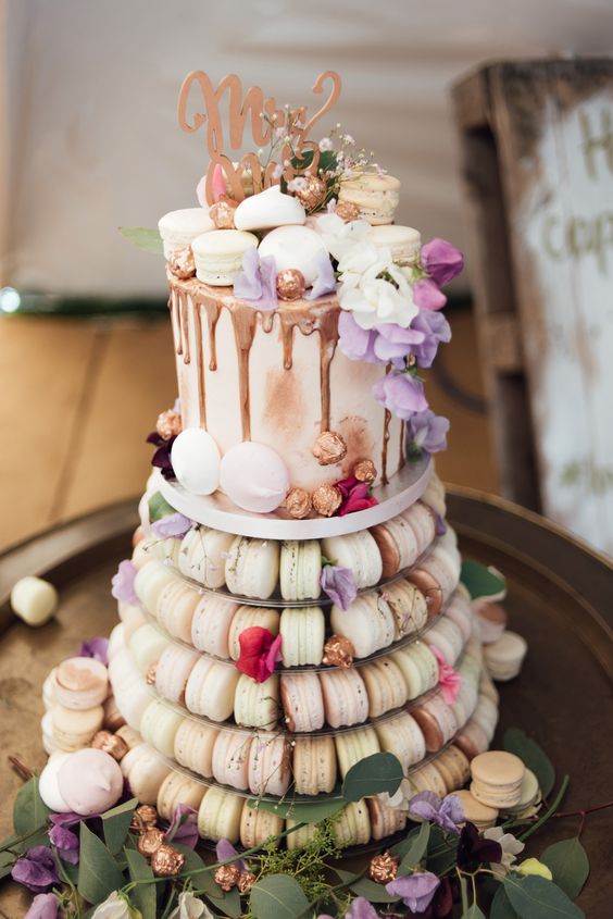 a macaron tower combined with a wedding cake topped with macarons and chocolate drip plus a topper
