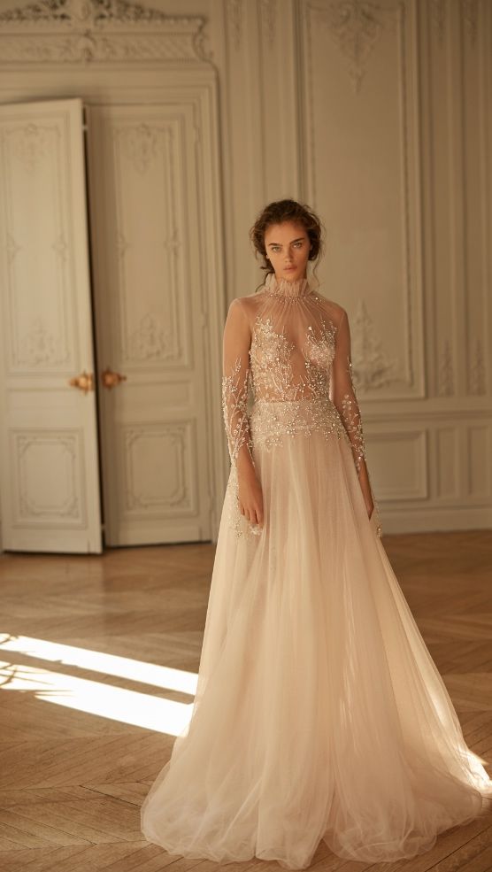 a beautiful and refined wedding dress with a sheer embellished and embroidered bodice, a layered skirt, a high neckline and long sleeves