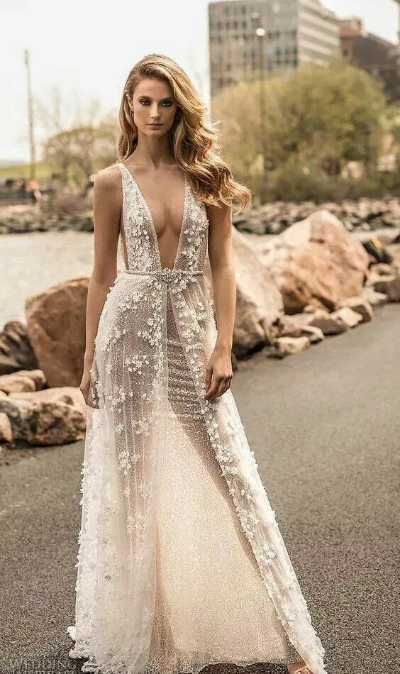 a naked wedding dress with a deep plunging neckline, lace applique all over, straps and an embellished belt for a daring bride