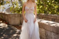 a strapless naked wedding dress with a sheer bodice with lace applique and embellishments and a layered skirt is gorgeous