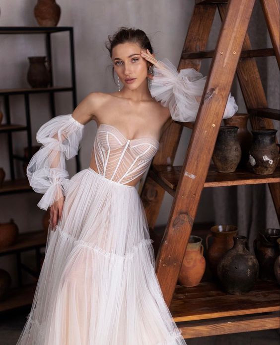 a unique strapless wedding dress with a sheer corset bodice and a layered skirt, some lseeves and side cutouts