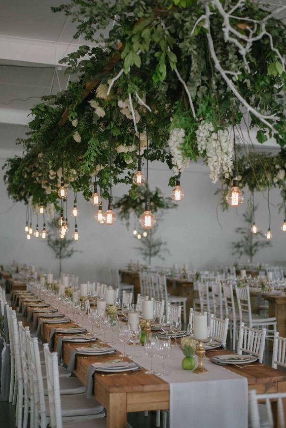 a lush greenery and white bloom installation with bulbs hanging down is a bold modenr decor idea