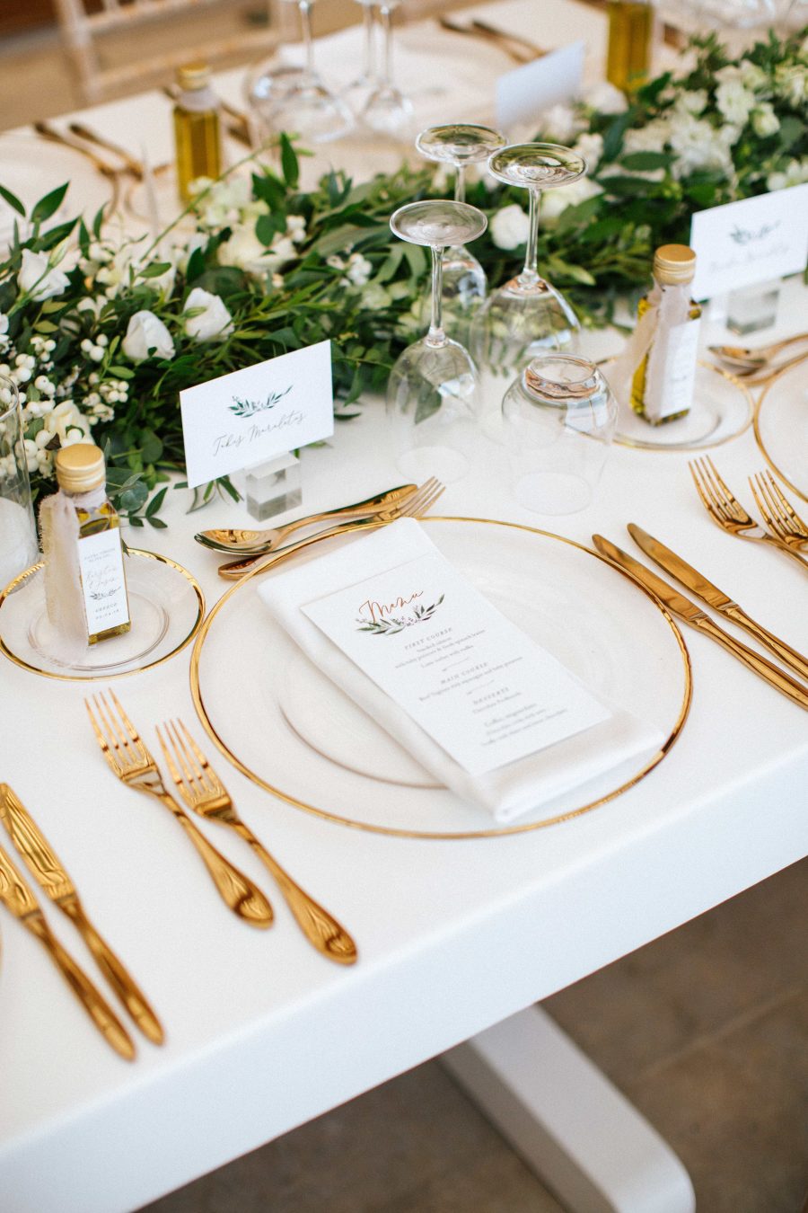 The wedding tablescape was neutral, with gold cutlery, with a greenery and white bloom table runner plus olive oil favors