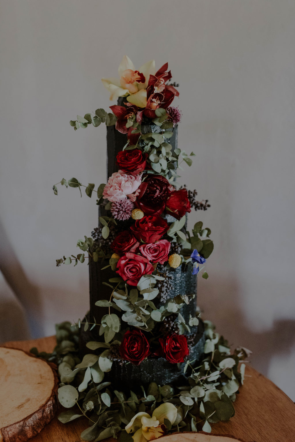 A textural black wedding cake with lush and bright florals was create by the bride