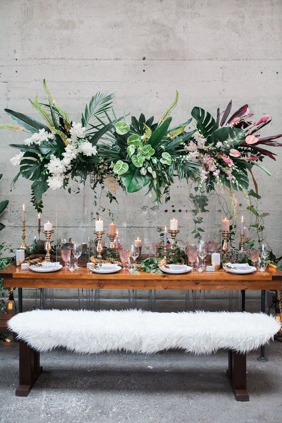 a lush tropical wedding installation with tropical leaves and blooms and some cascading greenery
