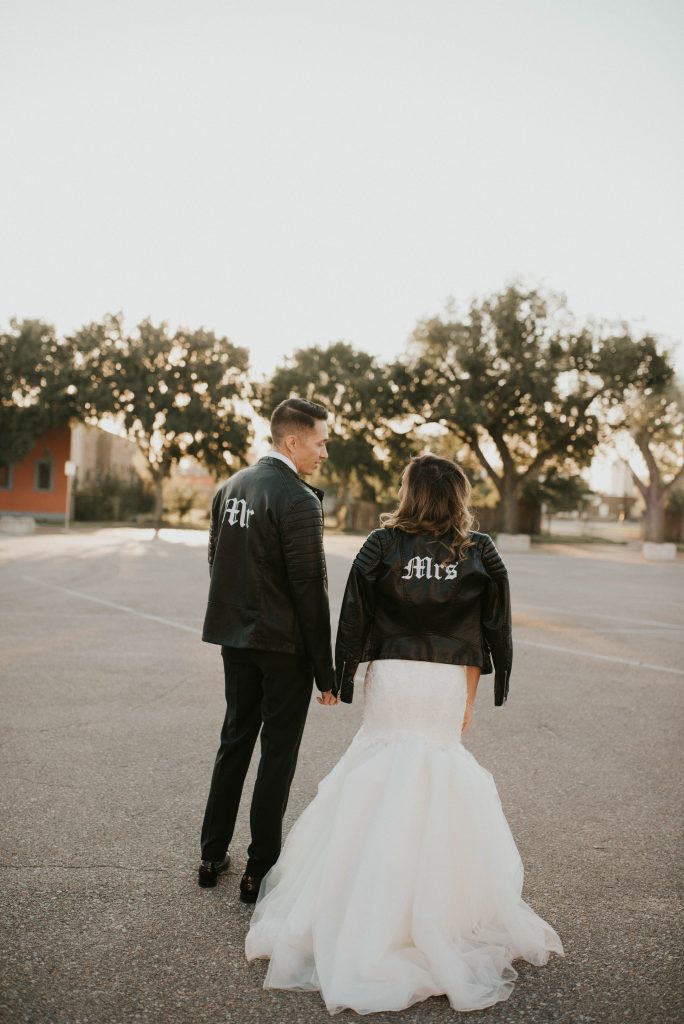 the groom and the bride wearing matching black leather moto jackets with handpainted details for a modern feel