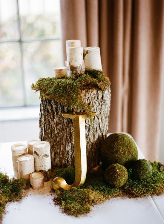 a woodland wedding centerpiece with a tree stump, moss balls and birch candle holders