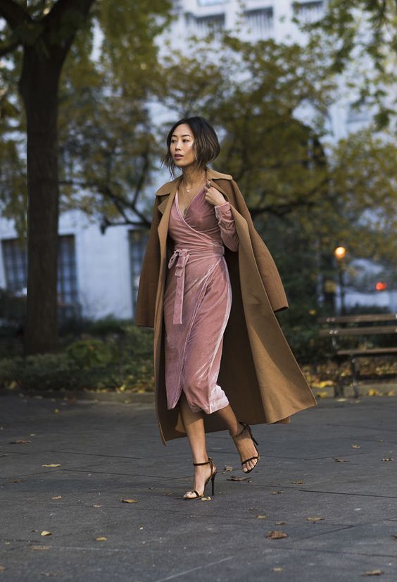 a pink wrap velvet dress with long sleeves and a V neckline, black heels and a camel coat