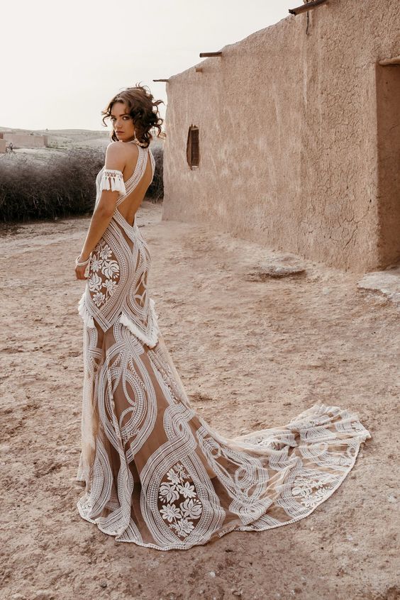 a nude wedding dress that incorporates tassel arm bands, tassles on the skirt and white lace