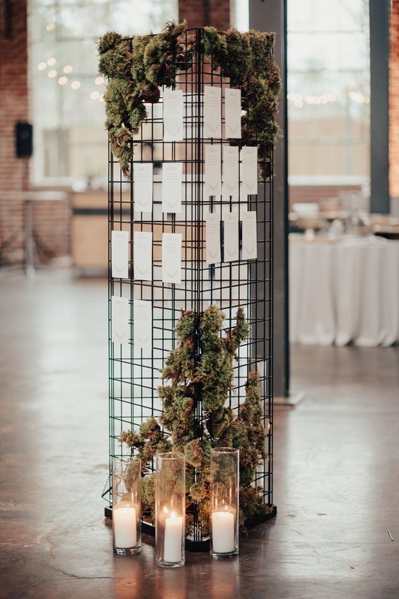 a modern wedding seating chart with moss, greenery and candles around is a stylish installation