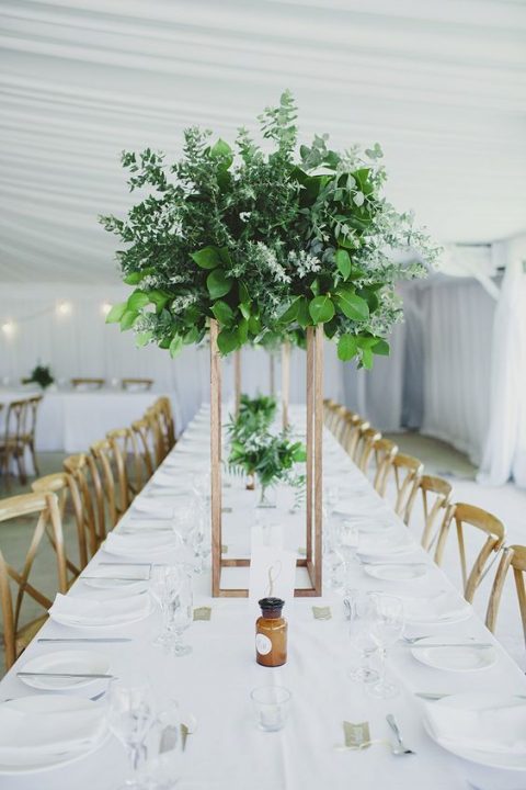 a tall greenery centerpiece of various types of eucalyptus and some foliage on a copper stand