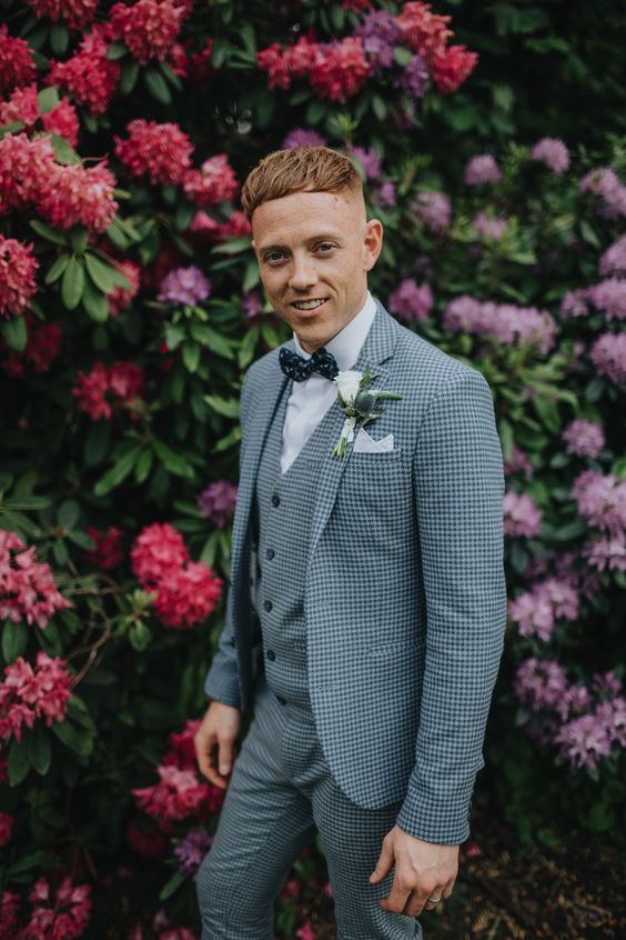 a checked blue three-piece suit, a white shirt, a navy polka dot bow tie plus a white floral boutonniere