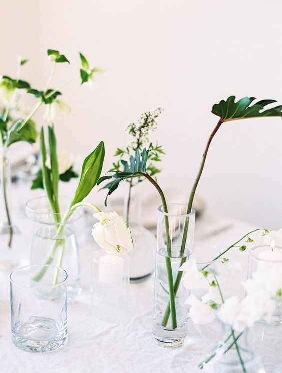 an arrangement of clear glasses with various leaves and some white blooms is a simple minimalist idea