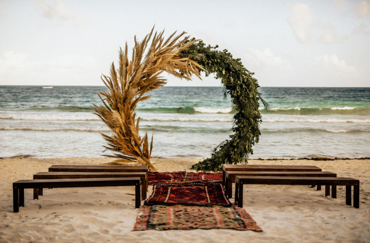 The wedding ceremony space was done with benches, boho rugs and a large circle wedding arch of pampas grass and greenery