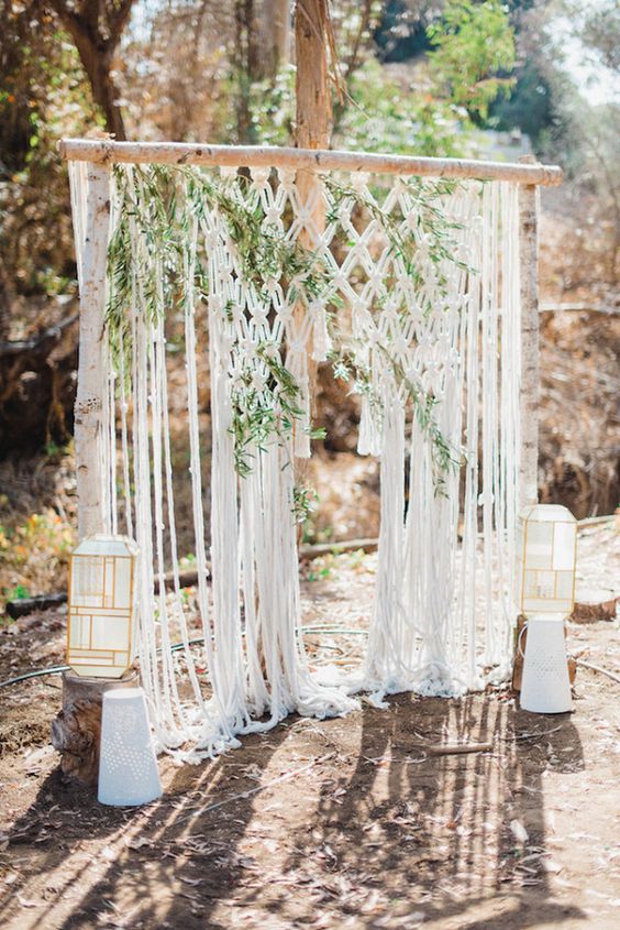 a cool macrame wedding backdrop with greenery interwoven and catchy geometric candle lanterns