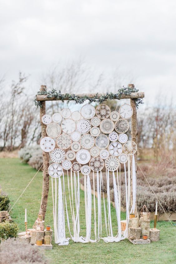 a rustic boho wedding backdrop made up of macrame dreamcatchers, greenery and candles around