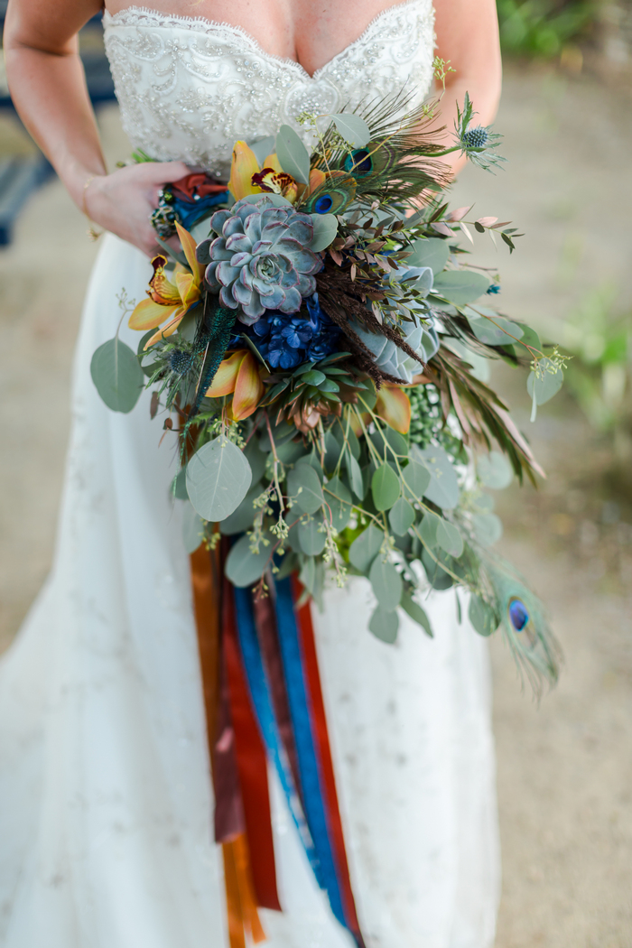 The wedding bouquet was done with lots of greenery, rust and blue flowers, succulents and even peacock feathers