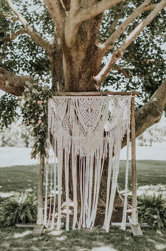 a relaxed summer wedding backdrop of macrame and some greenery and pink blooms hanging on one side
