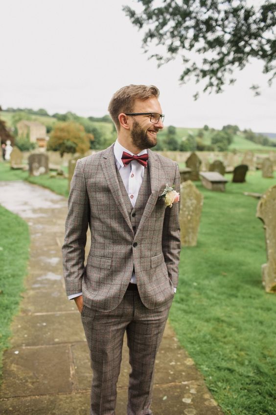 a stylish checked beige three piece suit, a white shirt with copper buttons, a burgundy bow tie