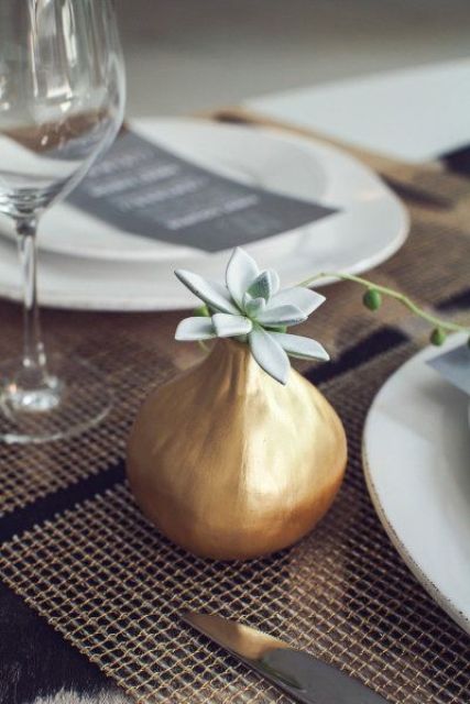 a pear-shaped gilded vase with a single pale succulent is a stylish and simple minimalist wedding centerpiece