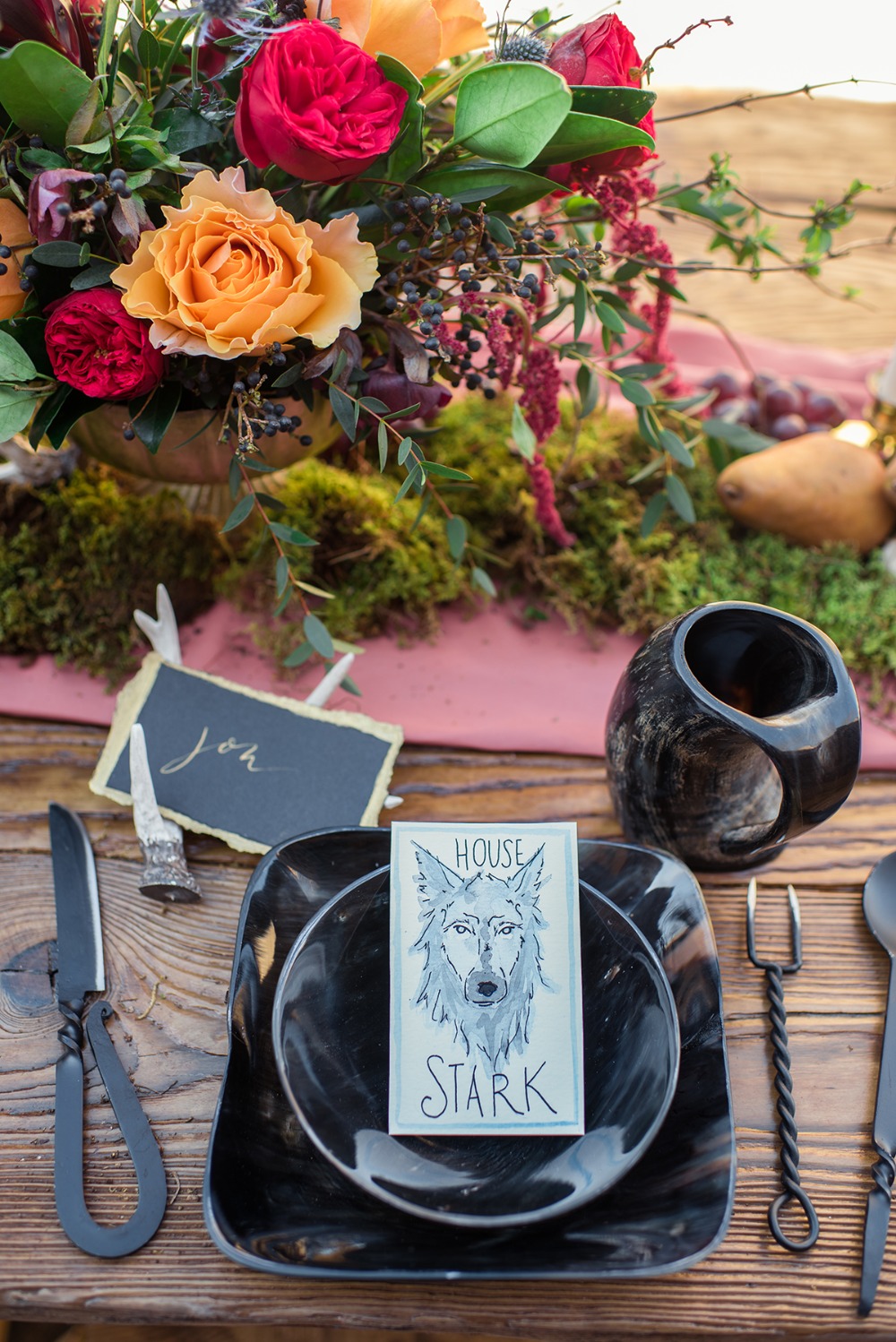 A unique and catchy wedding tablescape with black plates, unusual cutlery, a bright floral centerpiece and a moss runner