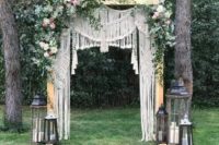 15 a boho macrame wedding arch with lush blooms and greenery on top plus candle lanterns around