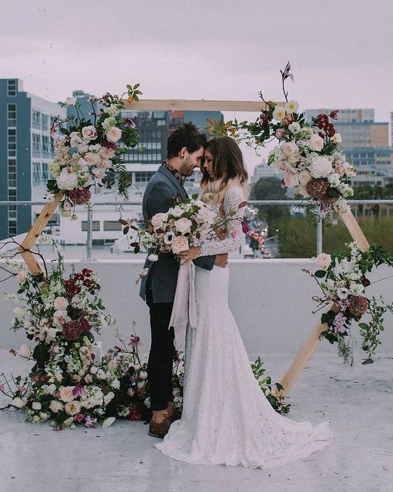 a hexagon wedding arch with super lush florals in pink, blush, burgundy and some leaves and branches