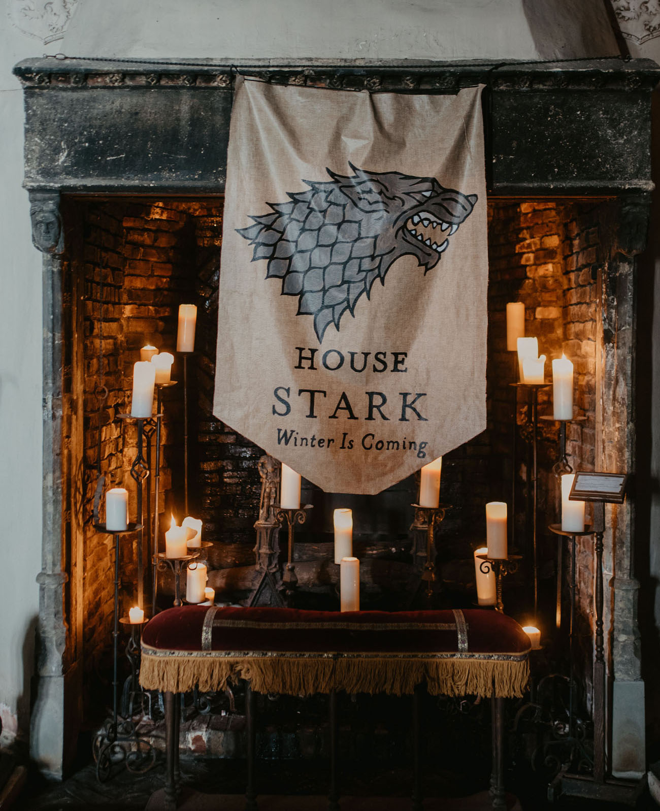 A unique wedding backdrop with a fireplace with candles, a velvet seat and a Stark flag