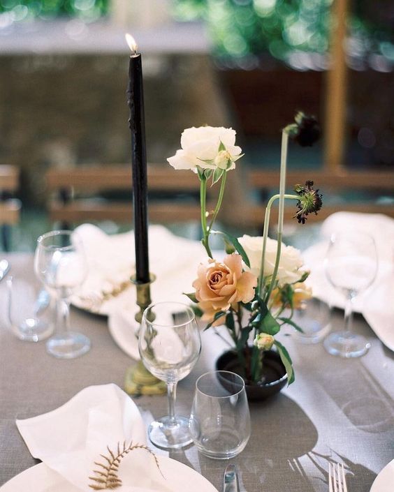 a delicate floral arrangement of a black vase, white and dusty pink blooms and a black candles in a gold candle holder