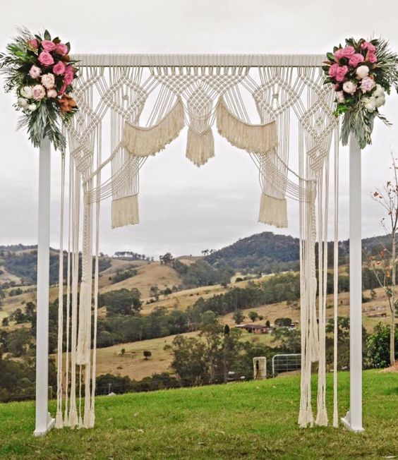 a bright macrame wedding arch with pink and blush blooms and greenery on the corners
