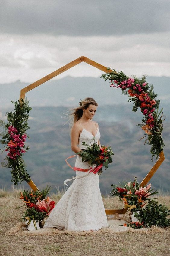 a bright polygon wedding arch decorated with pink blooms and lush greenery for a summer wedding