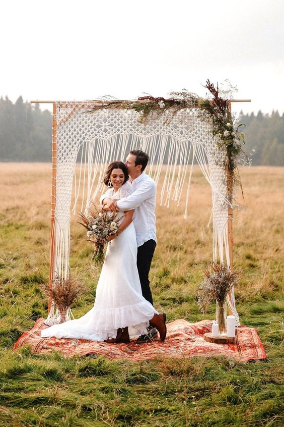 a fall boho wedding arch with macrame, some dried leaves and herbs plus white blooms, candles and dried herb arrangements