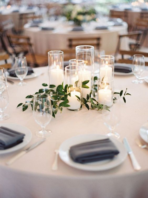 a group of candles with greenery is a chic minimalist wedding centerpiece that creates a cozy ambience at the table