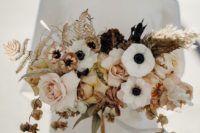 a chic wedding bouquet of white anemones, blush and dried roses, dried leaves, seed pods and dark foliage