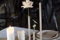 a chic white wedding tablescape with tall and thin vases and white orchids and roses, pillar candles and linens