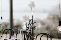a minimalist wedding centerpiece of black bud vases, white roses and leaves and a tall and thin candle