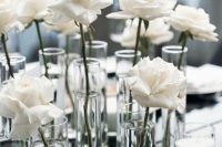a minimalist wedding centerpiece of glasses with single white roses and pillar candles is a cool and chic idea