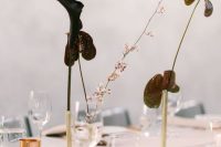 a minimalist wedding centerpiece of gold bud vases and dark anthurium plus blooming branches for a minimal wedding