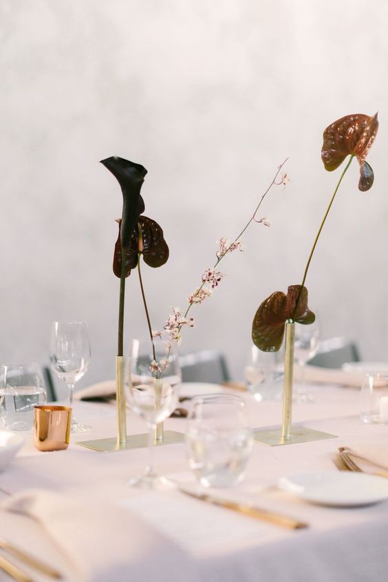 a minimalist wedding centerpiece of gold bud vases and dark anthurium plus blooming branches for a minimal wedding
