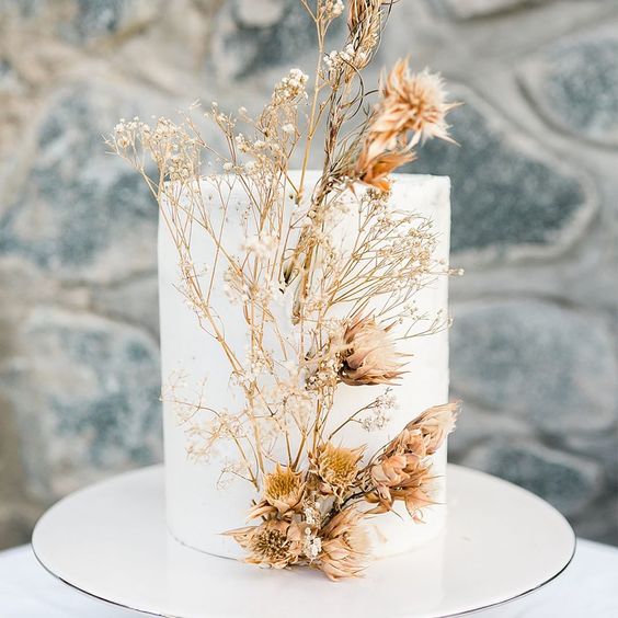 a minimalist white wedding cake decorated with dried blooms looks ethereal and very unusual, idela for the fall