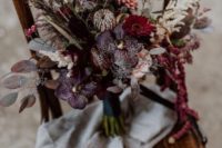 a moody fall wedding bouquet with dried foliage, herbs, burgundy, red and purple blooms features a catchy design